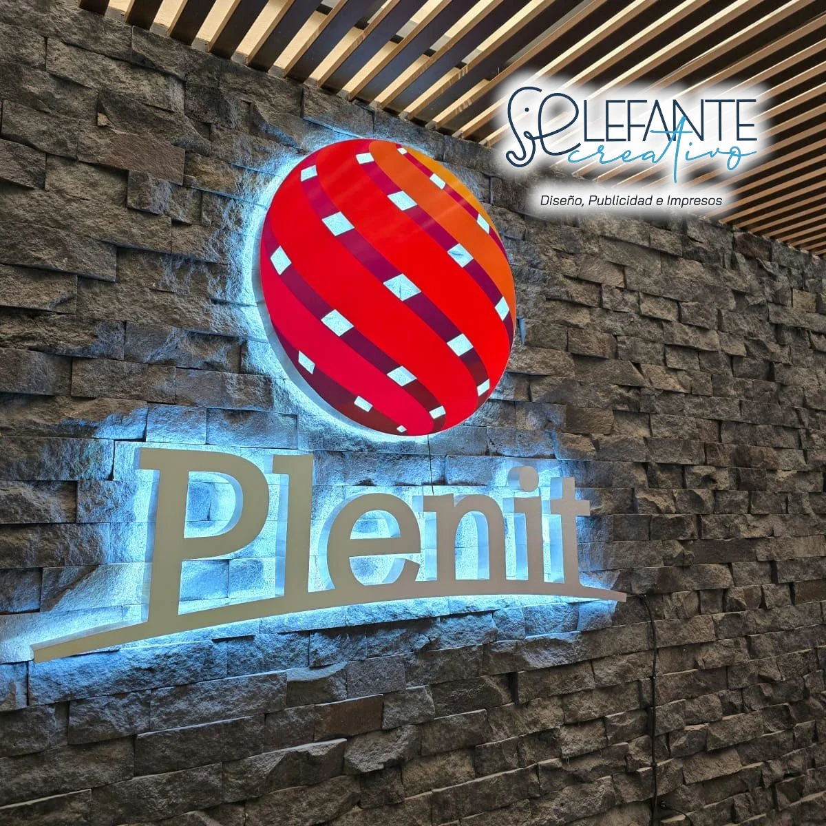 Anuncio tridimensional Plenit con iluminación azul sobre muro de piedra